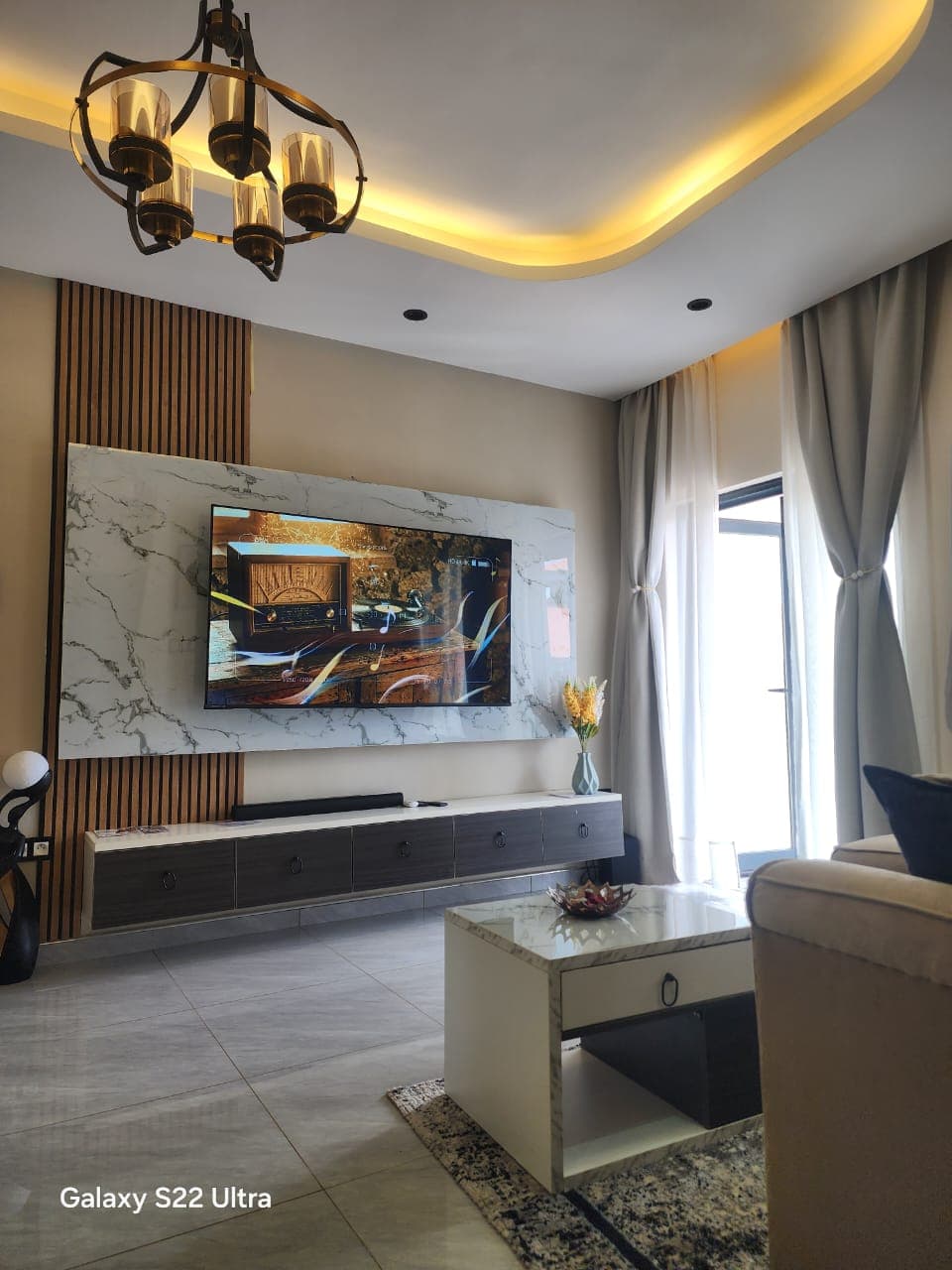 Salon avec mur TV en marbre, tasseaux bois et corniche LED